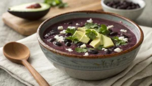 Purple Black Bean Soup in a rustic bowl with garnishes.